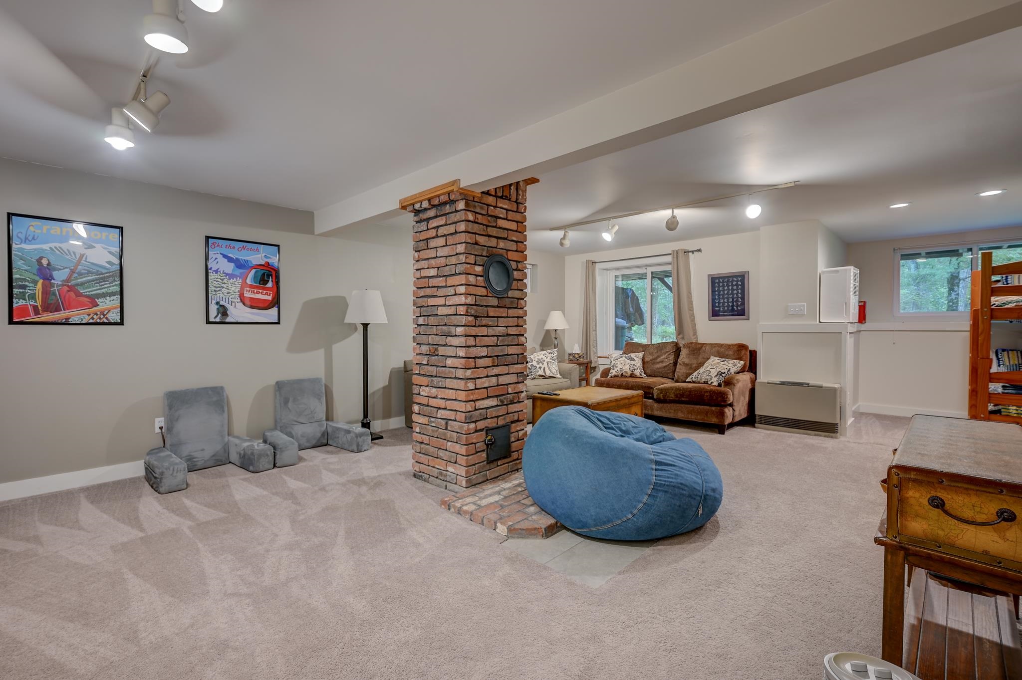 Furnished living room with a central brick chimney, blue beanbag, and ski posters.