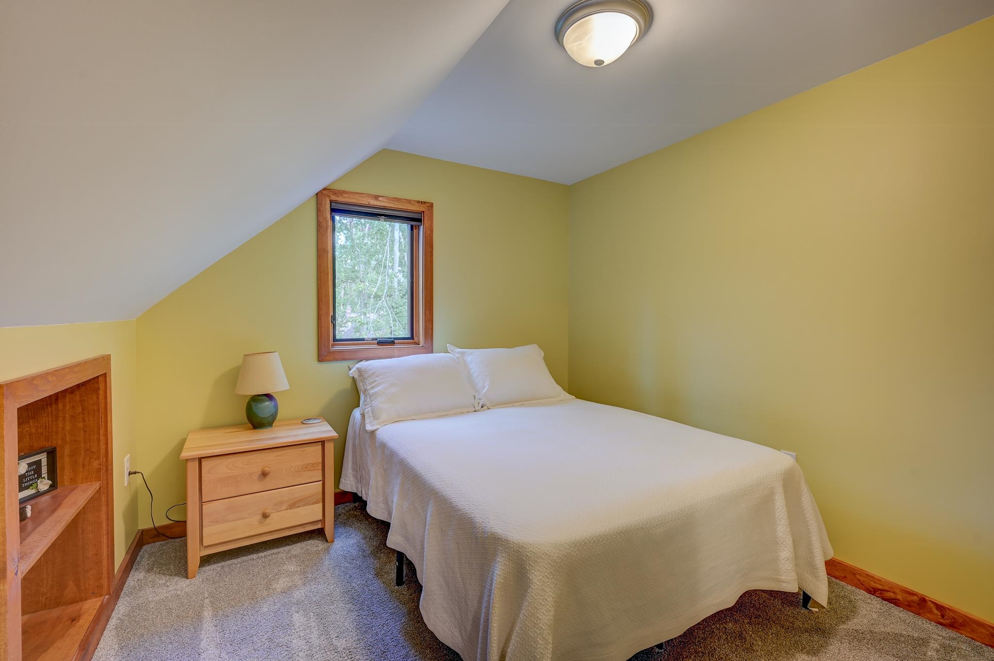 Attic bedroom with a white-covered bed, sloped ceiling, and wood-trimmed window.