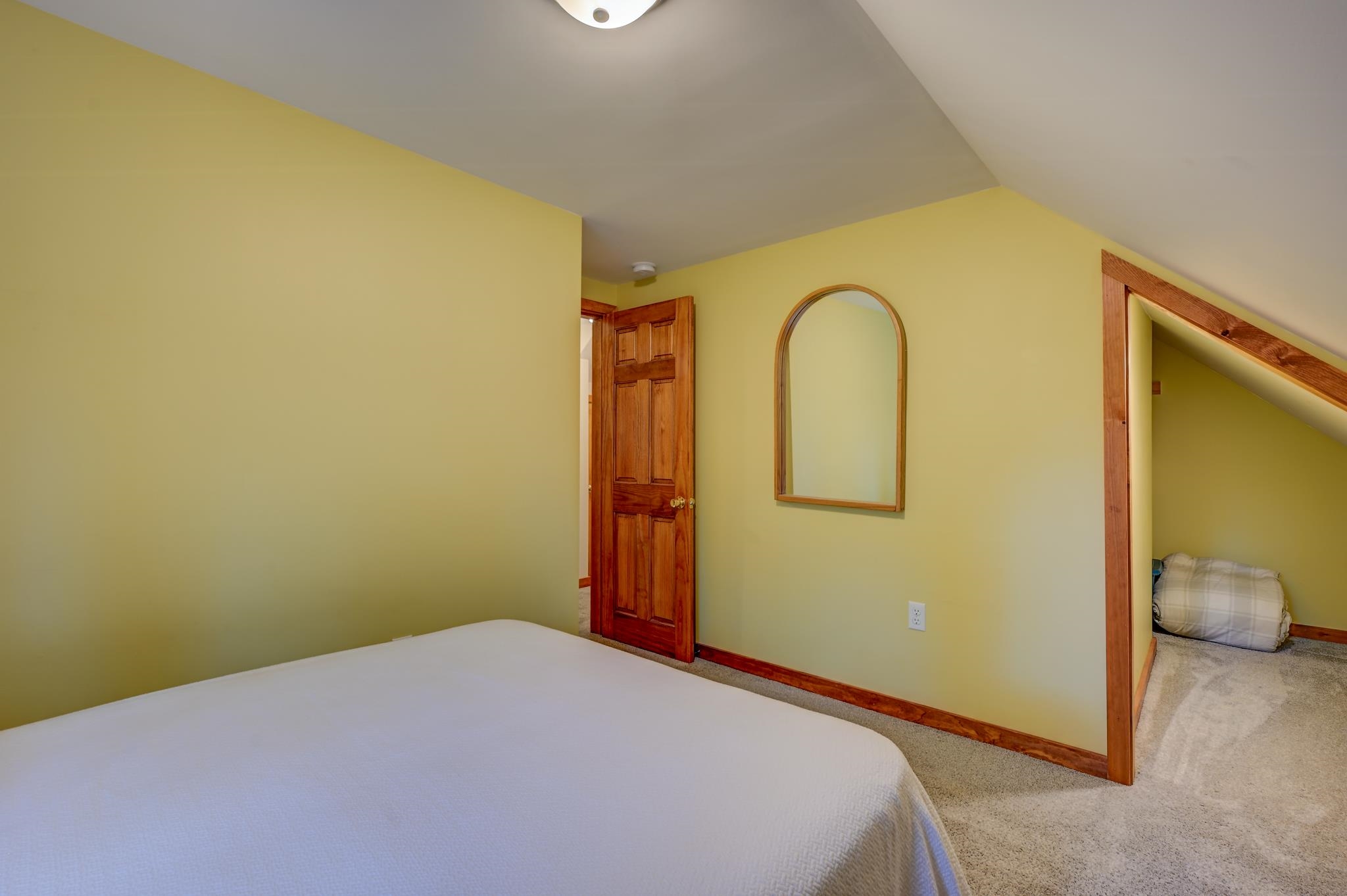 Bedroom with a sloped ceiling, wood trim, and a recessed sleeping nook beside the bed.