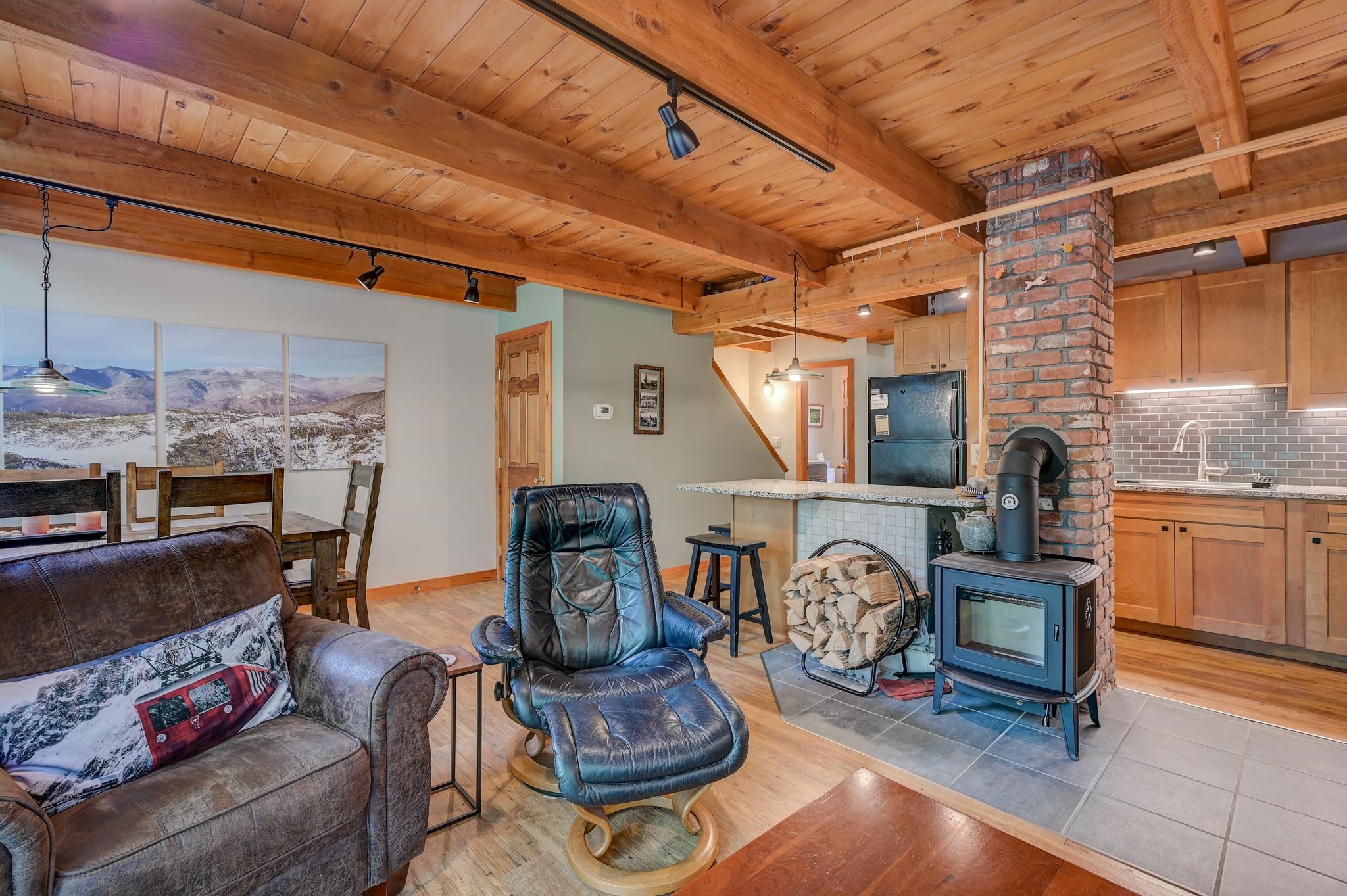 Open-plan living room and kitchen with exposed timber beams and a wood stove beside a brick chimney.