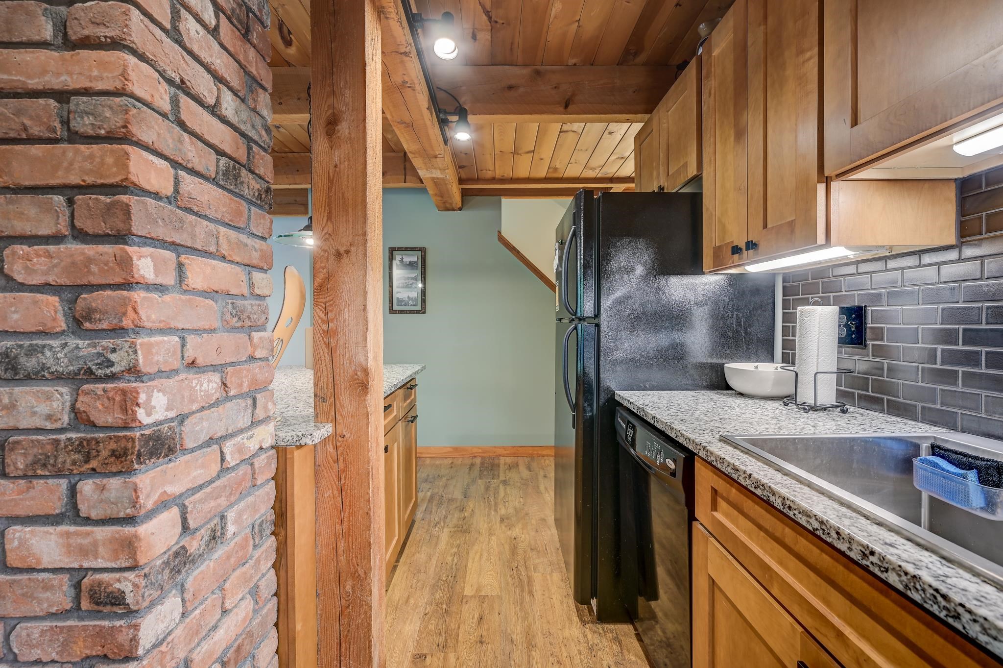 Kitchen with exposed wood beams, granite counters, gray tile backsplash, and a brick pillar