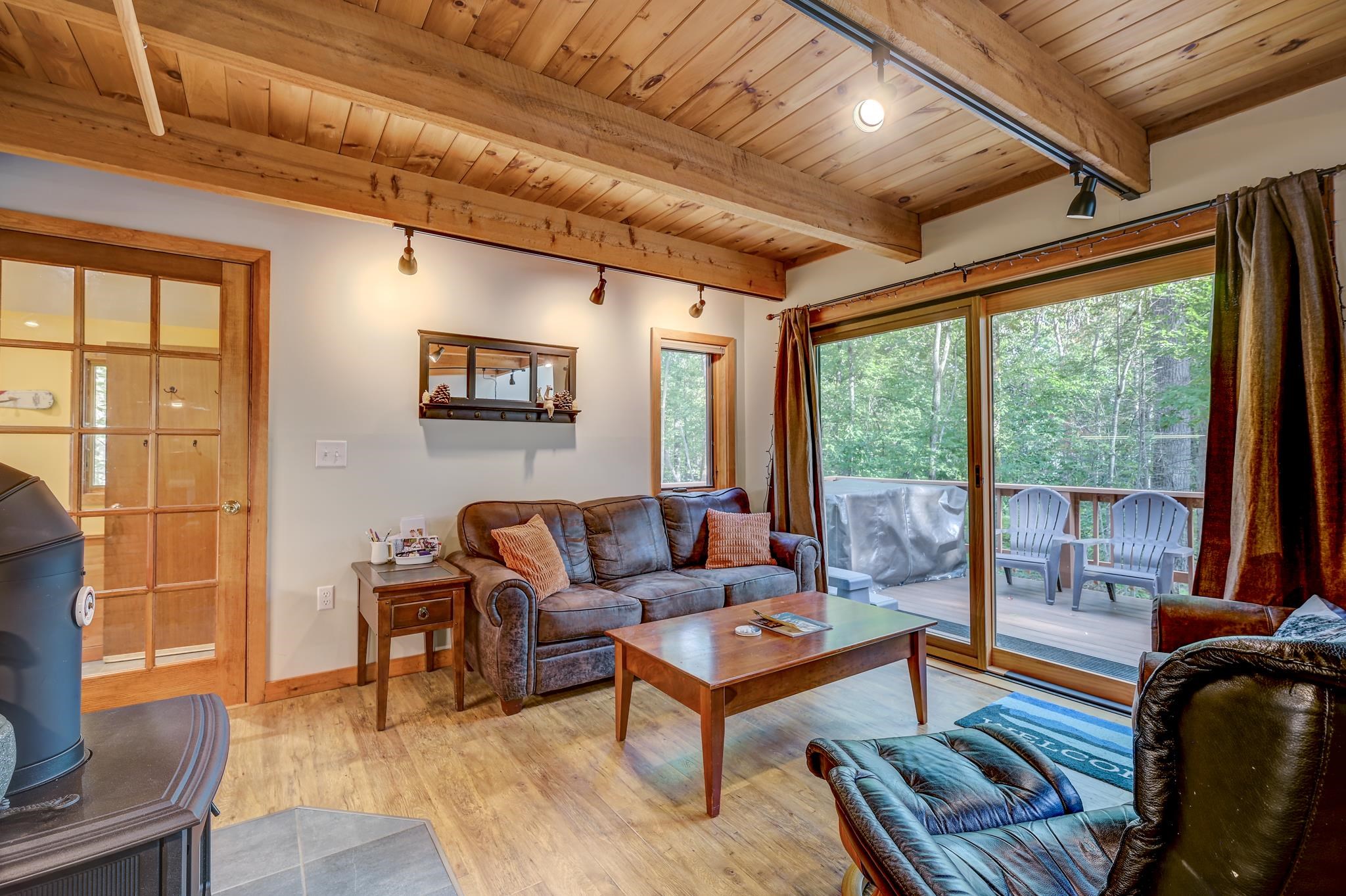 Living room with exposed wood beams, a wood stove, and sliding doors to a wooded deck.