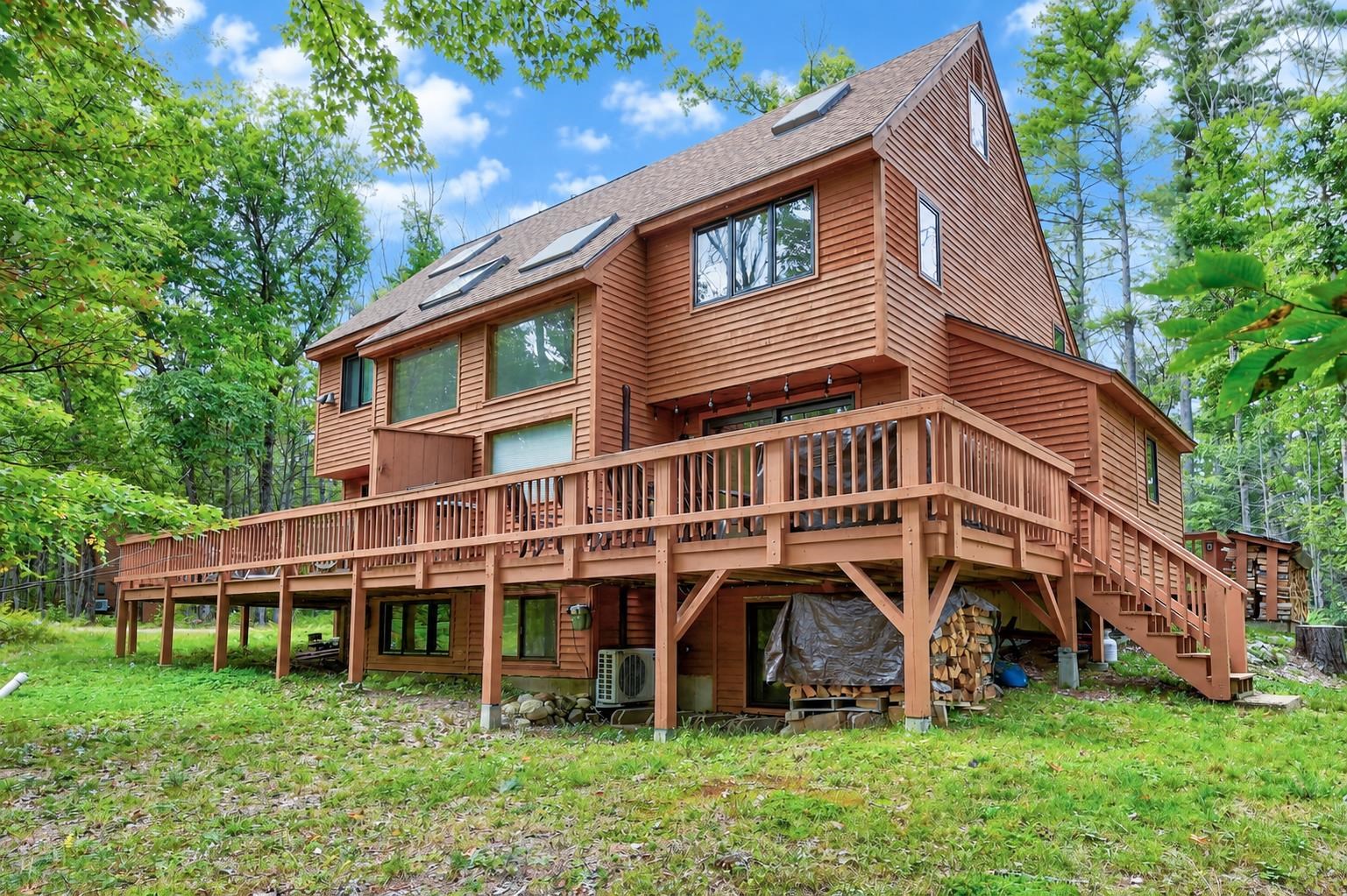 Wood-sided home with a large elevated deck and exterior stairs, surrounded by trees.