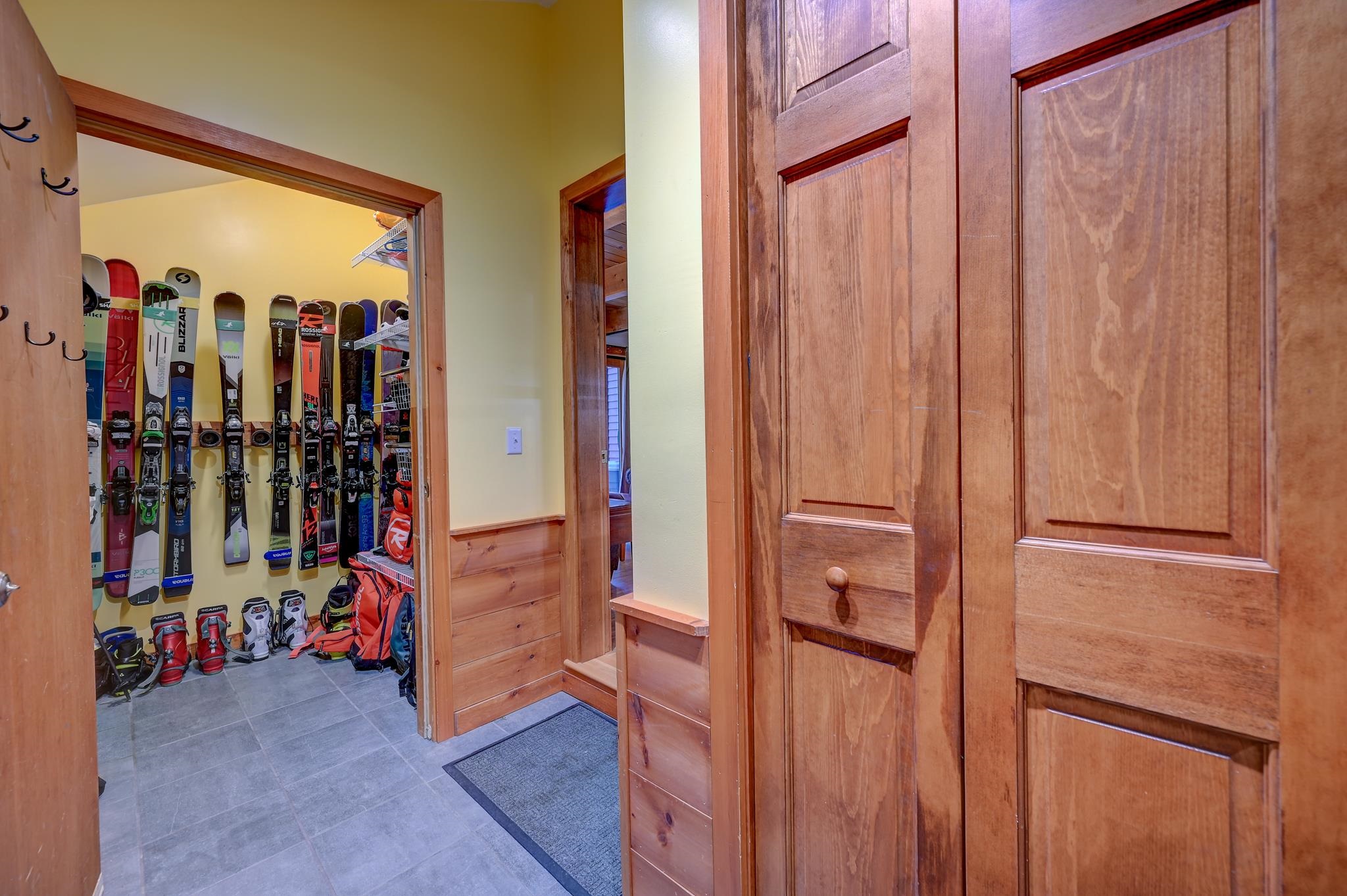 Ski storage room with skis and boots on racks beside wood-paneled entry cabinets.