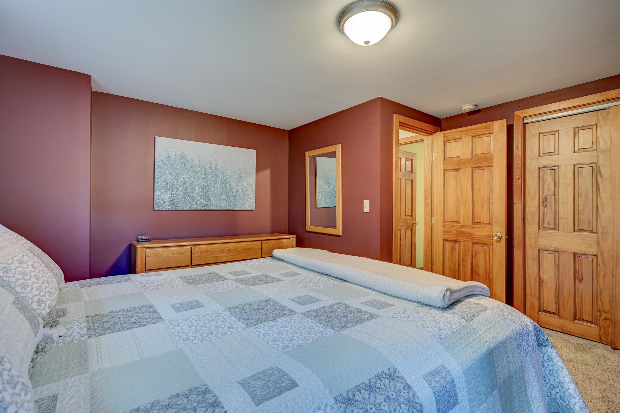 Bedroom with a blue-and-white quilted bed, burgundy walls, and light wood doors.