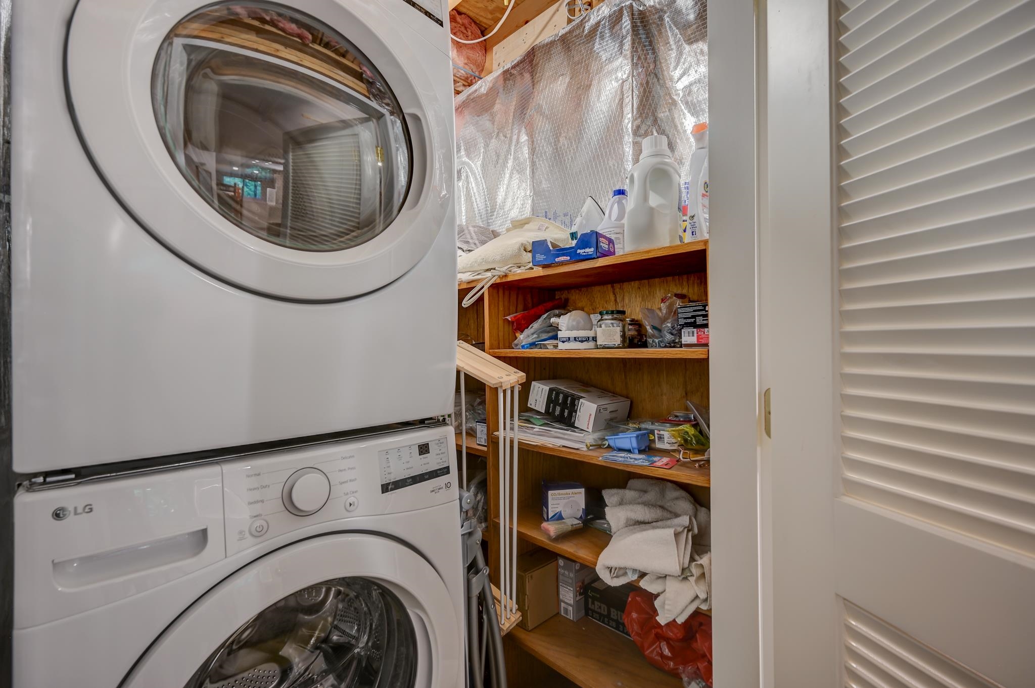Laundry room with stacked washer and dryer beside open shelving stocked with household supplies.