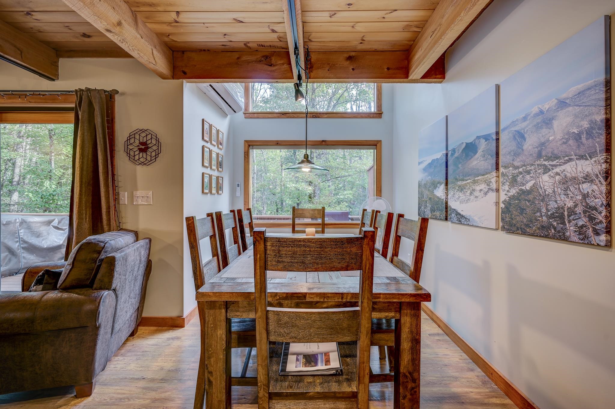 Dining area with exposed timber beams, a wooden table, and large windows overlooking trees.