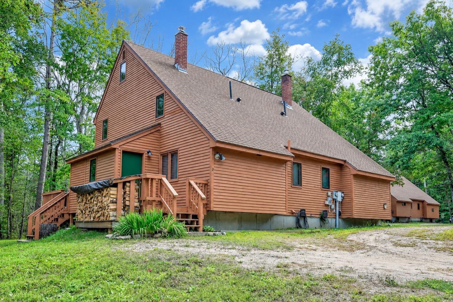 Brown wood-sided home with a steep roof, brick chimneys, and a raised deck among trees.