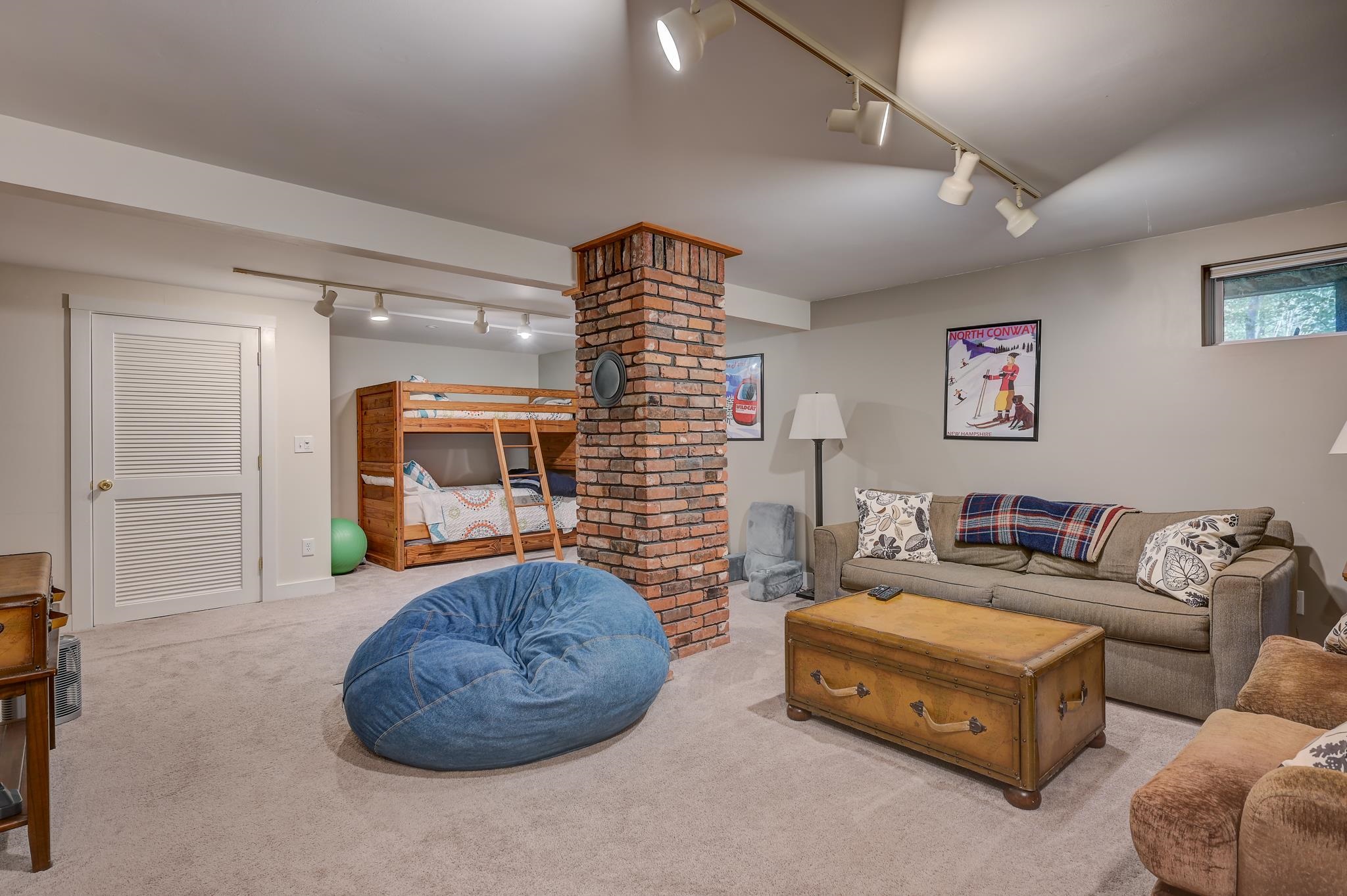 Furnished basement recreation room with bunk beds and a brick column dividing the seating area.