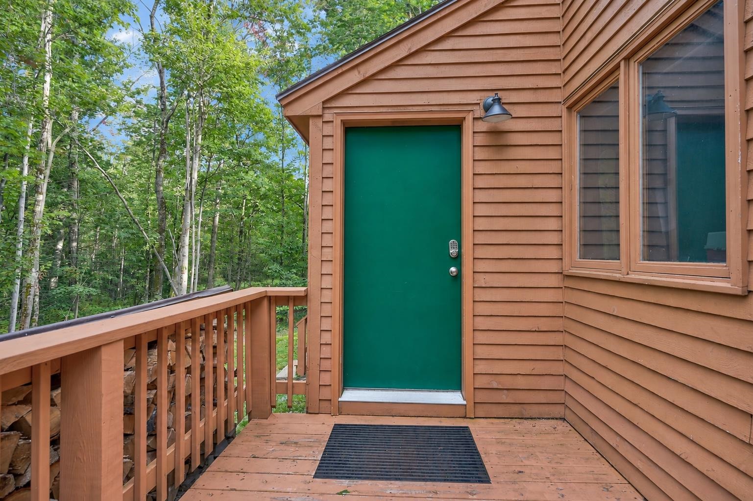 Home entry with a green door and wooden deck surrounded by leafy trees.