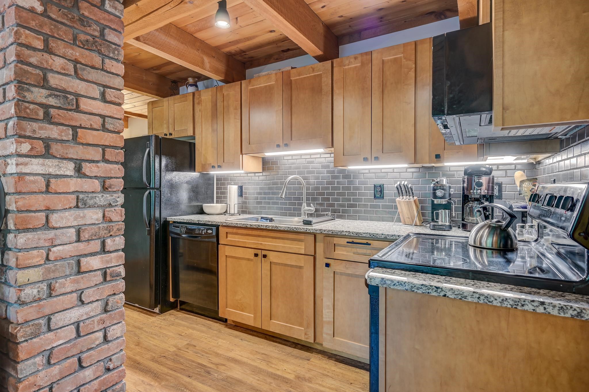 Kitchen with light wood cabinetry, gray tile backsplash, granite counters, and exposed timber ceiling beams.