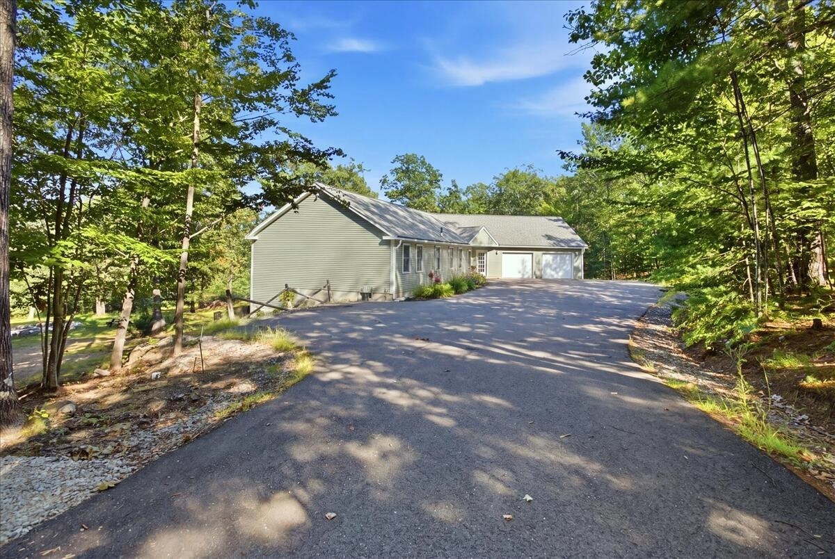 Ranch home with attached garage and broad driveway, surrounded by leafy trees.