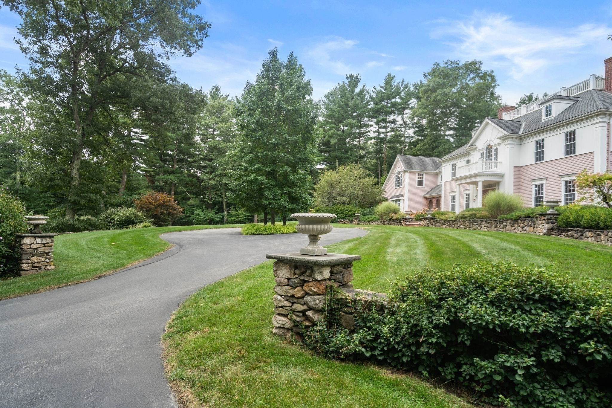 Large pink-and-white home beside a curved driveway, manicured lawn, and stone garden walls.