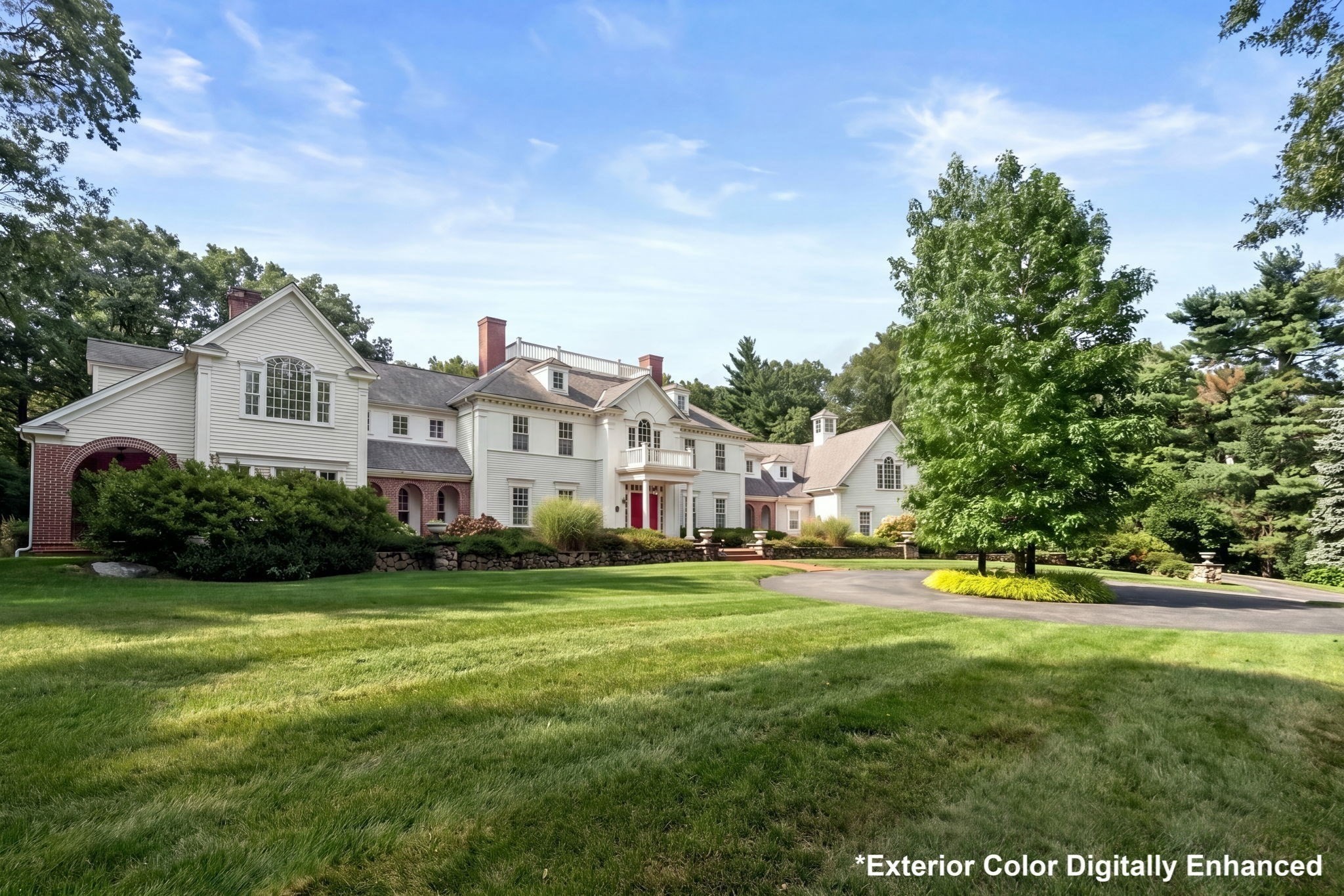 Large white house with red brick accents, landscaped lawn, mature trees, and a curved driveway.