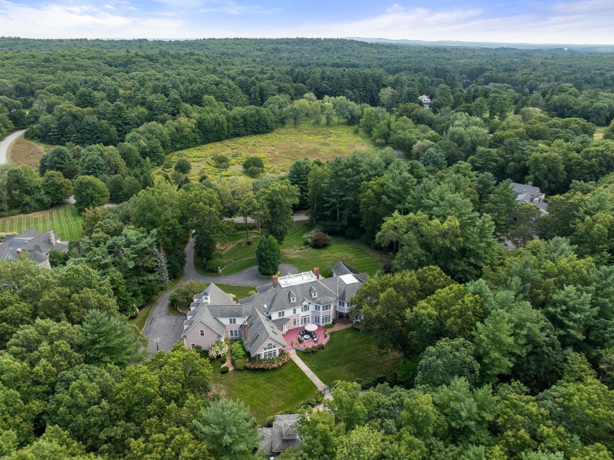 Aerial view of a large home amid wooded grounds, with a curved driveway and broad forest clearing.