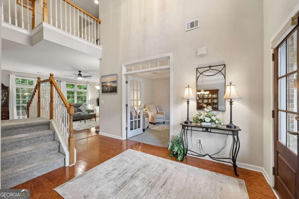 Two-story foyer with a carpeted staircase, hardwood floors, and an adjoining sitting room.