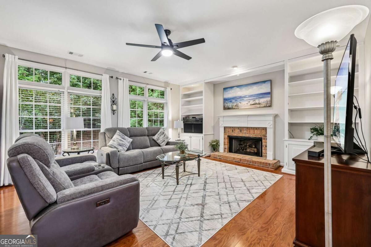 Living room with gray sofas, a brick fireplace, built-in shelving, and large windows.