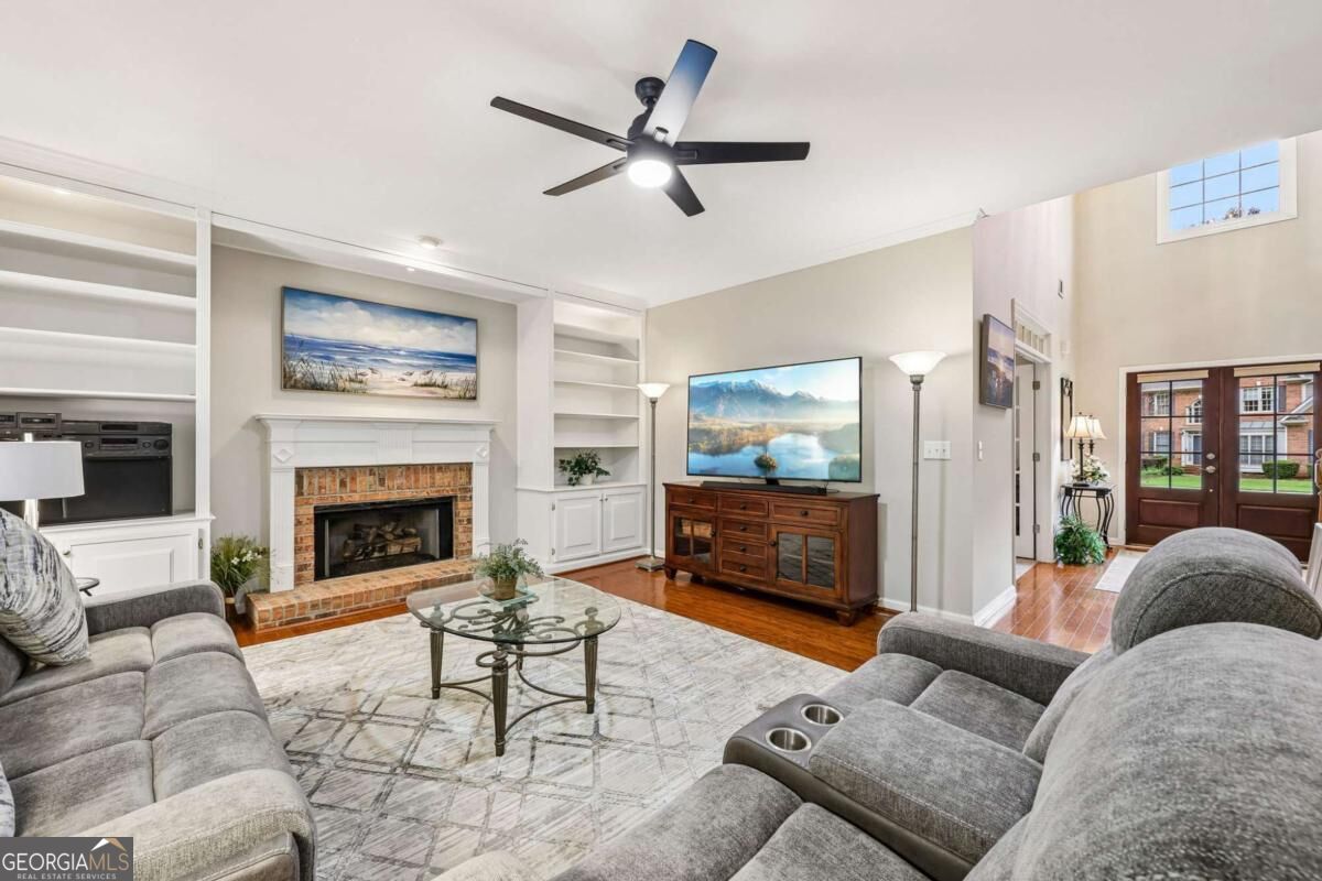 Living room with gray sectional sofas, brick fireplace, built-in shelves, and French doors.