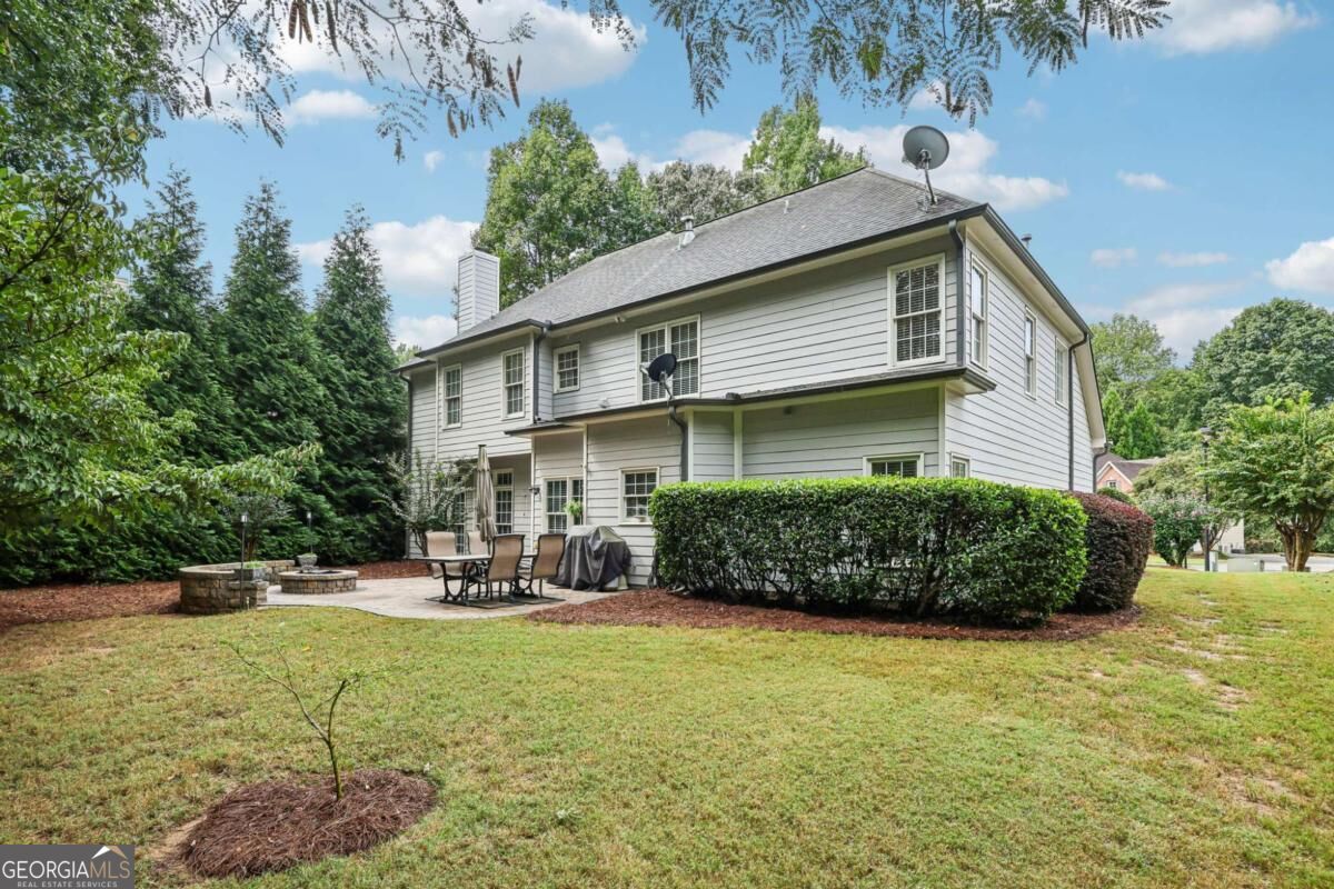 Rear of a two-story gray house with a patio, hedges, and a broad lawn.