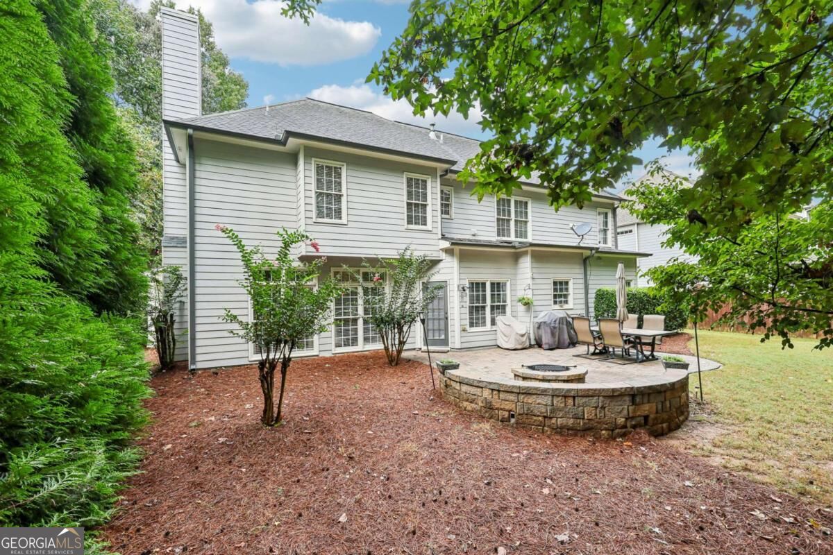 Two-story gray house with a stone fire pit patio and outdoor dining set in the backyard.