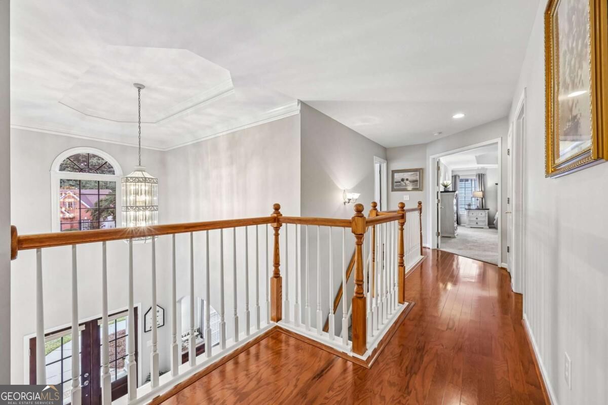 Upstairs hallway with polished hardwood floors, wood-and-white railing, and an arched window overlooking the foyer.