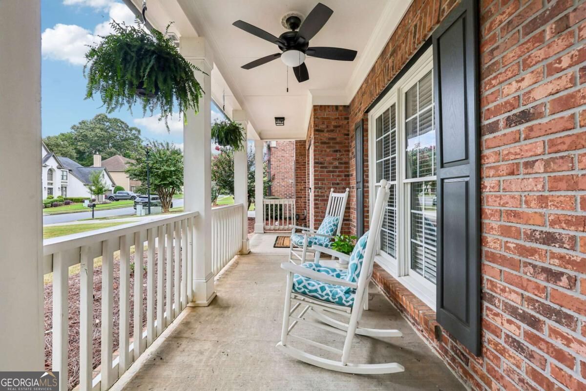 Covered brick front porch with white rocking chairs, hanging ferns, and a view of the residential street.