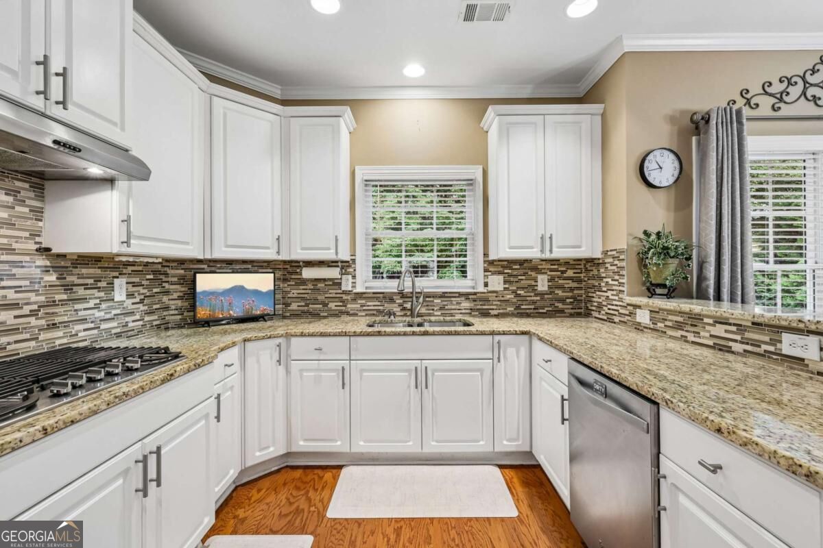 Kitchen with white cabinets, granite counters, multicolored tile backsplash, and a sink beneath a window.