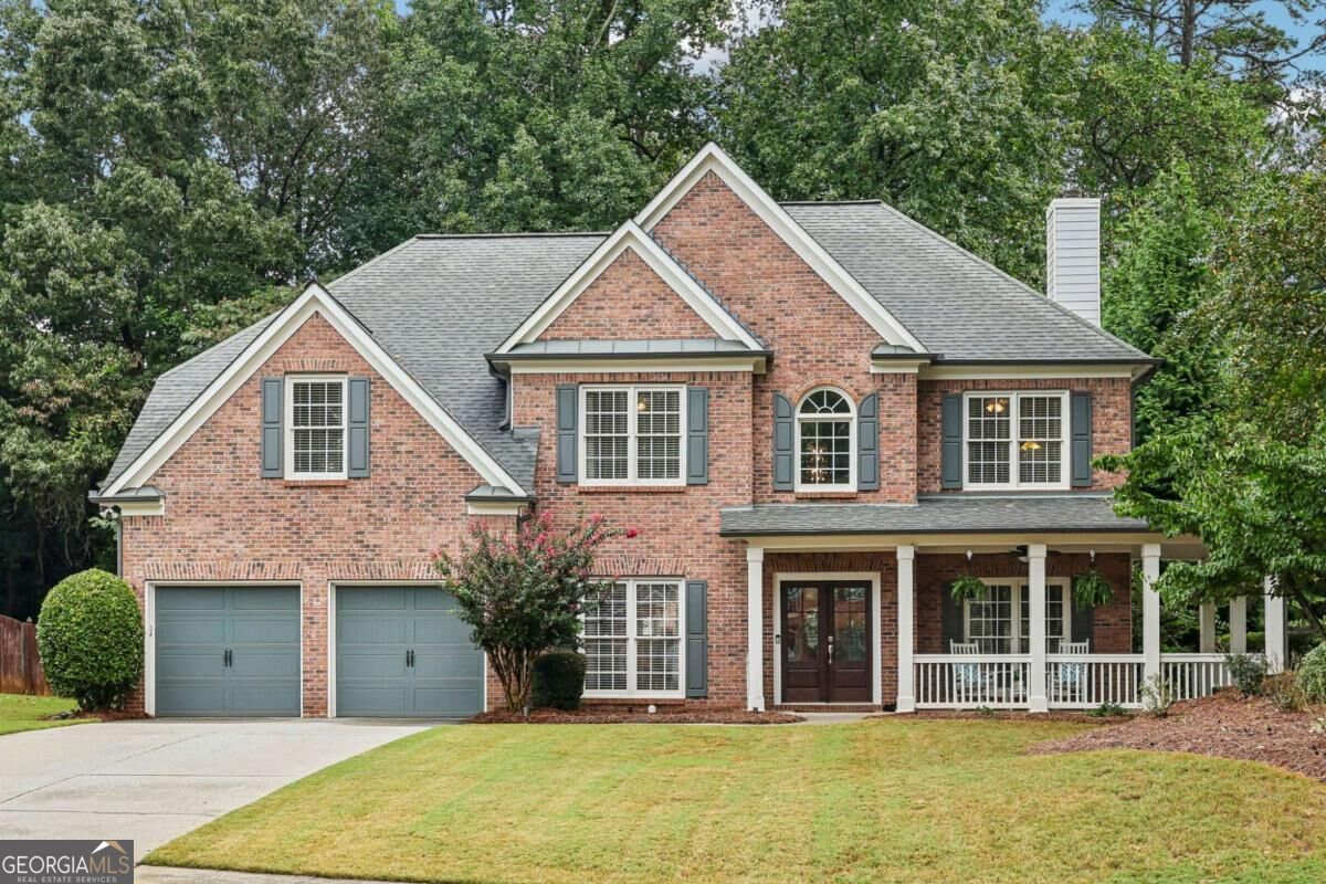 Two-story red brick home with a covered porch, double garage, and mature trees.