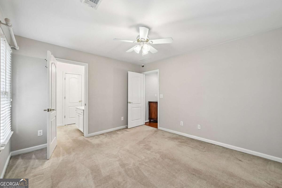 Unfurnished bedroom with beige carpet, a ceiling fan, and open doors.