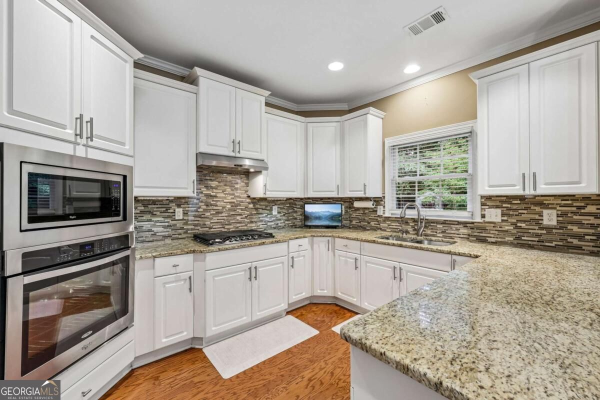 Bright kitchen with white cabinets, granite counters, mosaic backsplash, and stainless steel double oven.