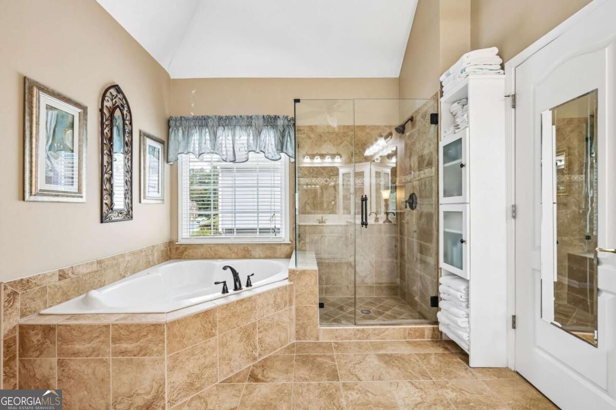 Bathroom with a corner soaking tub, tan stone tile, and a glass-enclosed walk-in shower.