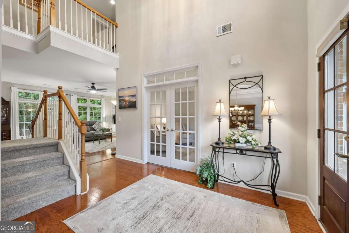 Two-story foyer with a carpeted staircase, hardwood floors, and French doors.