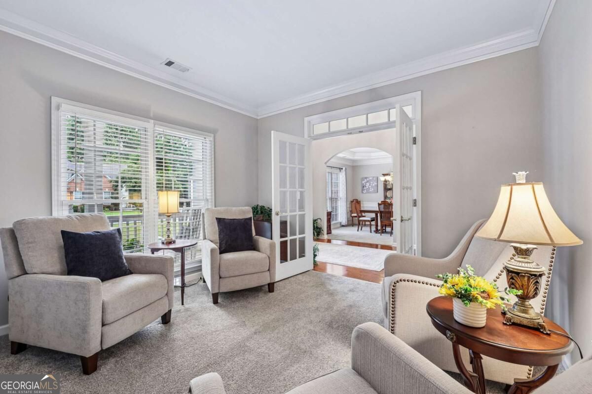 Living room with gray armchairs, large blinded windows, and French doors opening to a dining room.