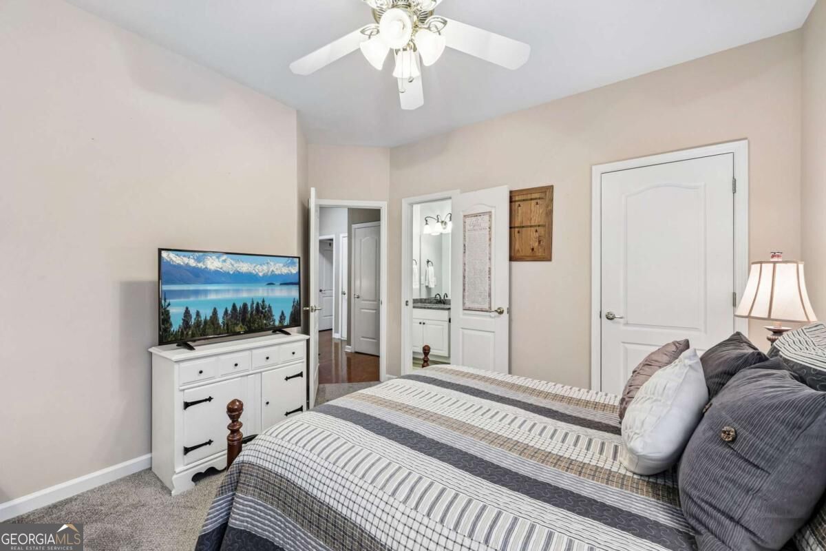 Furnished bedroom with striped bedding, a television on a white dresser, and an open doorway to the bathroom.