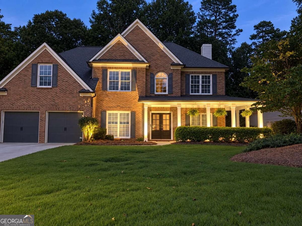 Brick two-story home with a covered porch and double garage, illuminated at dusk.