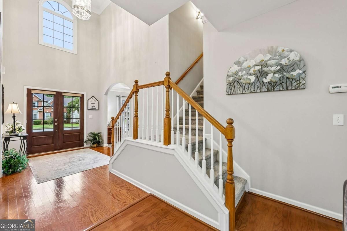 Two-story foyer with hardwood floors, double front doors, and a carpeted staircase with wood handrails.