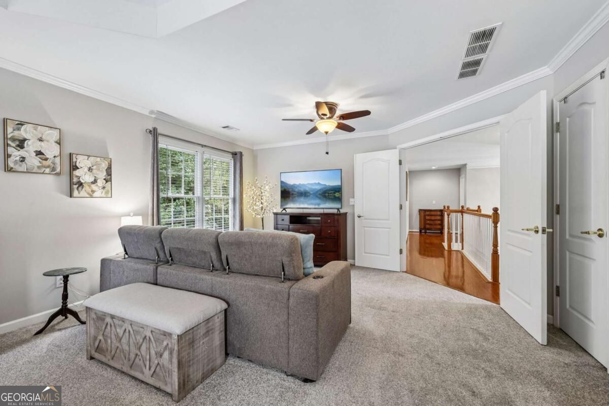 Upstairs living room with a gray sectional, ceiling fan, and open doors to a hardwood landing.