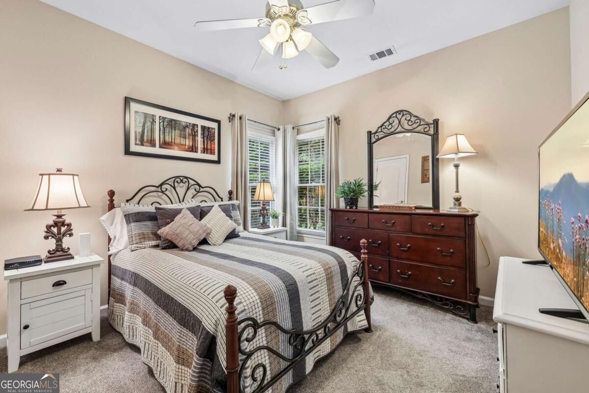 Bedroom with wrought-iron bed, striped quilt, dark wood dresser, and two tall windows.