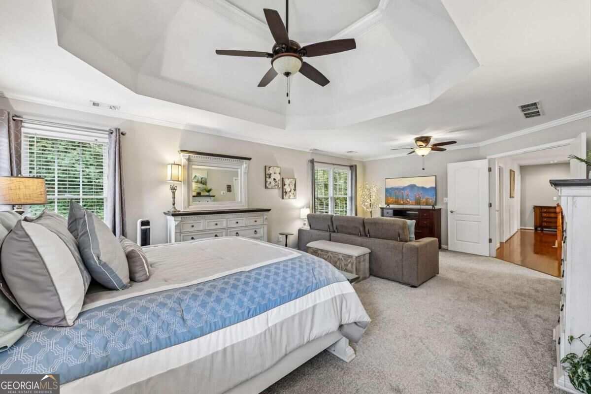 Furnished bedroom with a tray ceiling, large bed, sitting area, and ceiling fans.