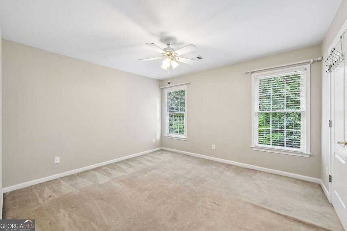 Empty carpeted bedroom with two windows and a ceiling fan.