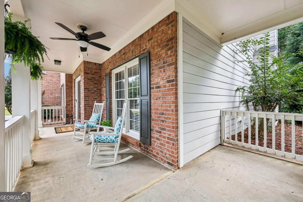 Covered brick porch with two blue-cushioned rocking chairs and a ceiling fan.