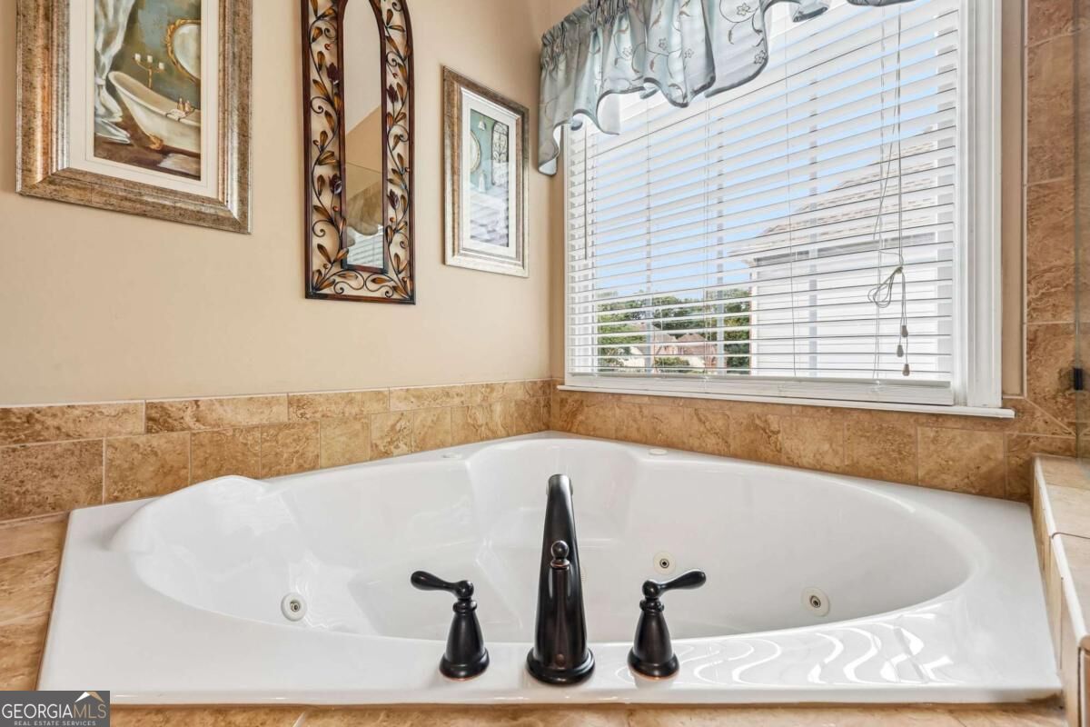 Corner soaking tub with dark fixtures, tan tile surround, and a wide window.