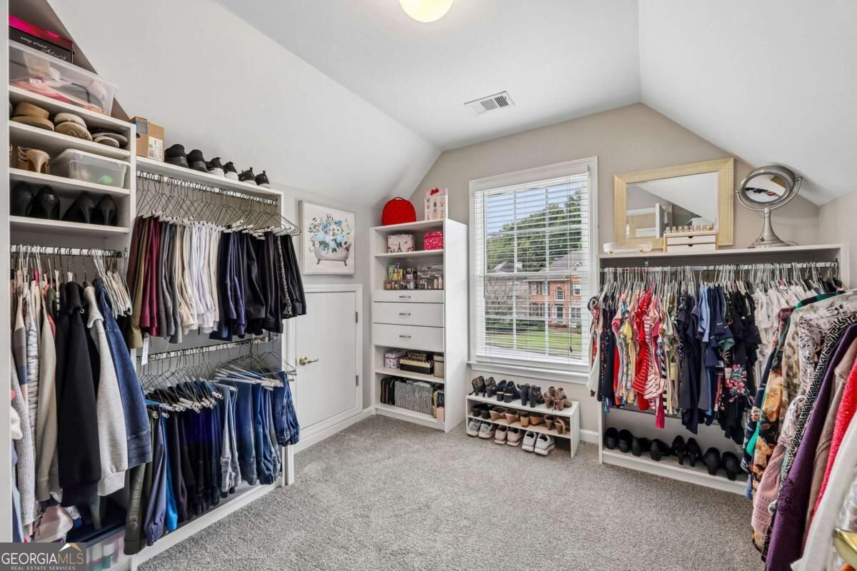 Walk-in closet with extensive clothing storage, shoe shelves, and a window overlooking a neighboring home.
