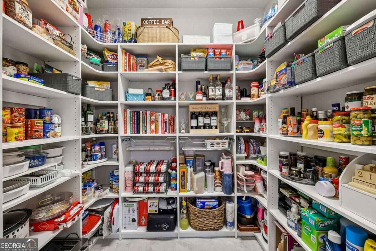 Walk-in pantry with fully stocked white shelves, woven baskets, and a coffee bar sign.