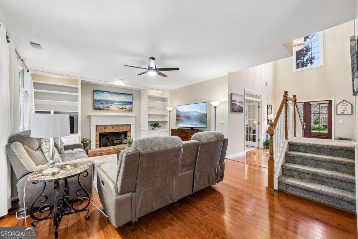 Living room with gray recliners, a brick fireplace, built-in shelves, and a staircase.