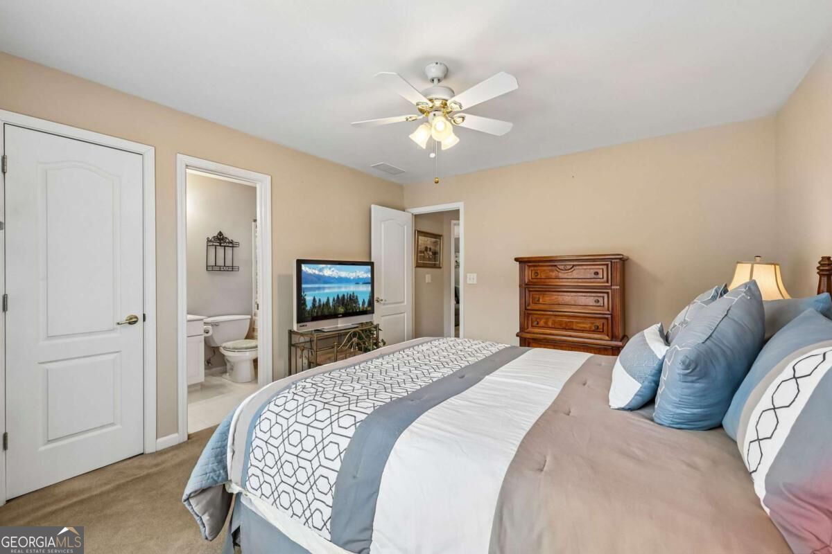 Furnished bedroom with blue and white bedding, wooden dresser, television, and doorway to an attached bathroom.
