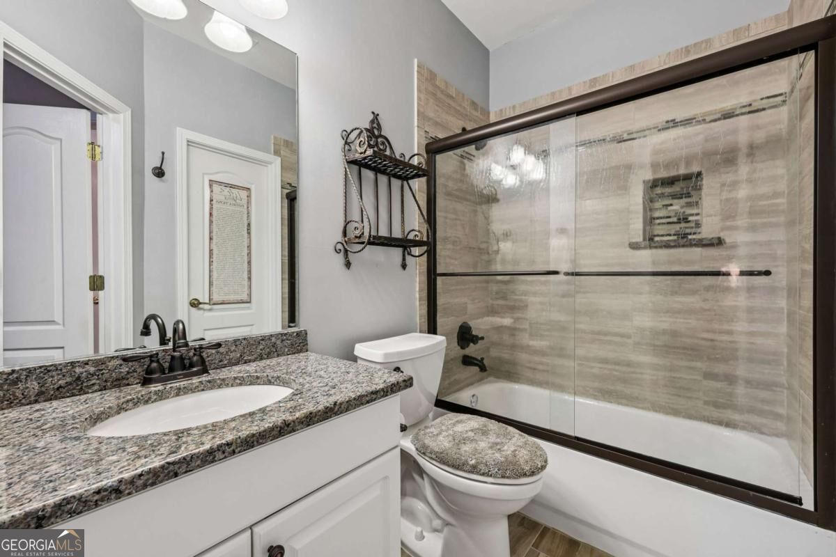 Bathroom with granite vanity and glass-enclosed tub featuring beige tile and dark trim.
