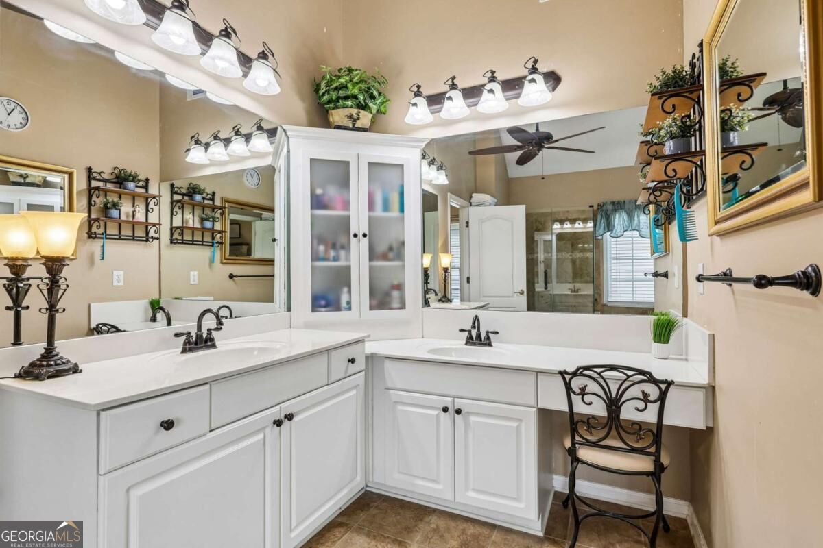 Bathroom with a white two-sink vanity, wall-to-wall mirrors, and a black metal chair.
