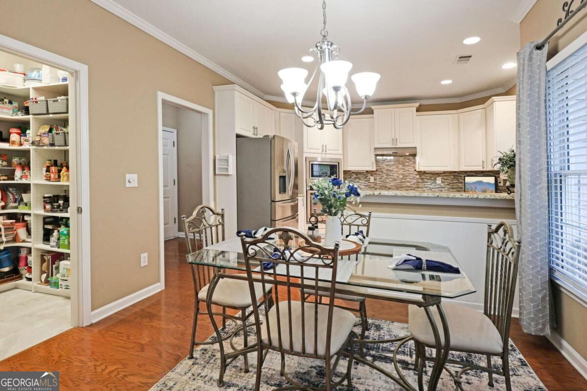 Kitchen and dining area with white cabinets, stainless appliances, and a glass table beside an open pantry.