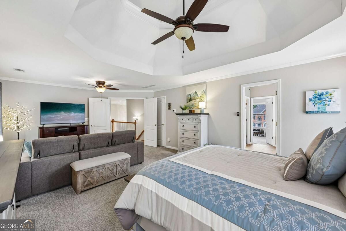Furnished bedroom with a large bed, gray sofa, and vaulted tray ceiling.